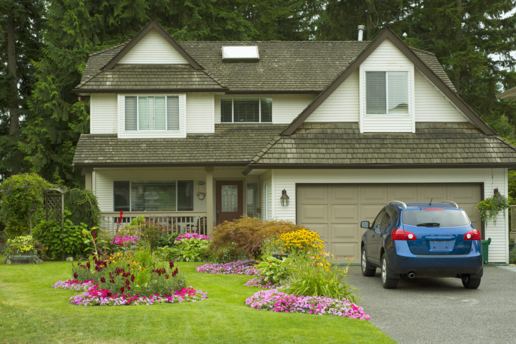 Front of a house, with a well manacured garden and lawn with a blue car