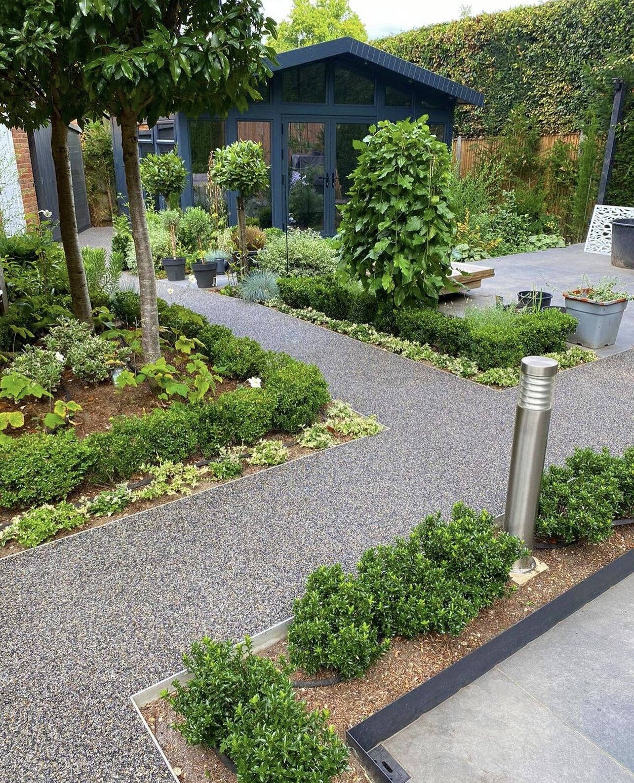 Modern garden design featuring metal-edged pathways, lush greenery, and a dark blue garden room.