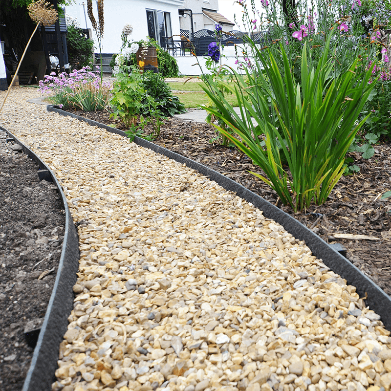 Curved gravel pathway with black plastic edging surrounded by a vibrant flower bed.